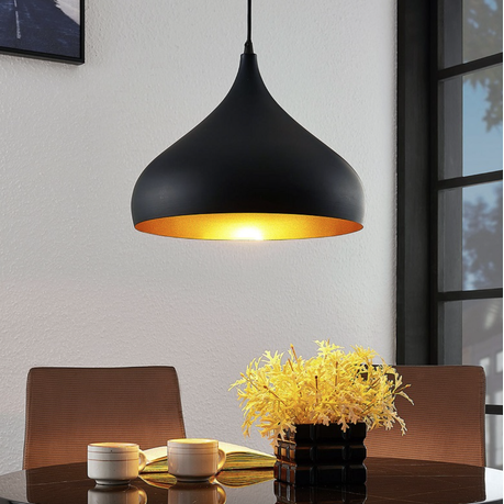 Black pendant light with gold interior hanging above a dining table with chairs and a vase of yellow flowers.